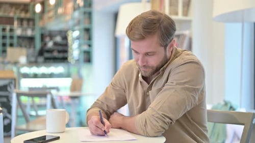 Serious Young Man Doing Paperwork in Cafe