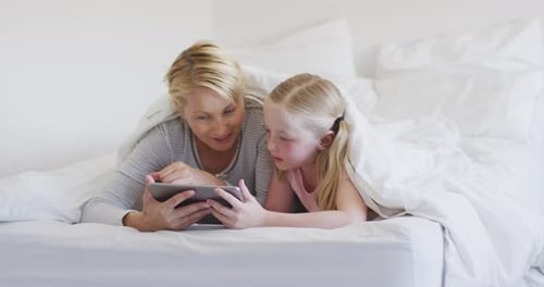 Vista frontal de una mujer caucásica y su hija usando una tableta digital en la cama