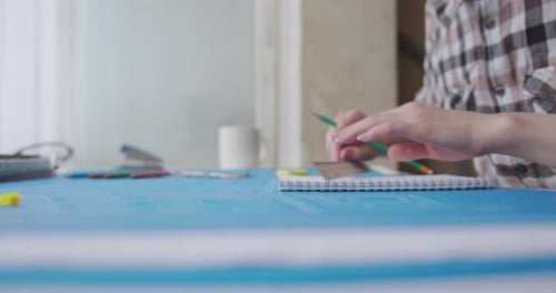A young woman works and studies architecture from blueprints. She draws with a pencil in a notebook