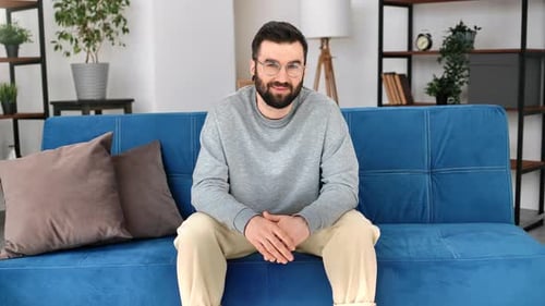 Erfolgreicher brutaler Mann freundlich lächelnd auf der Couch sitzend posiert komfortables Zuhause