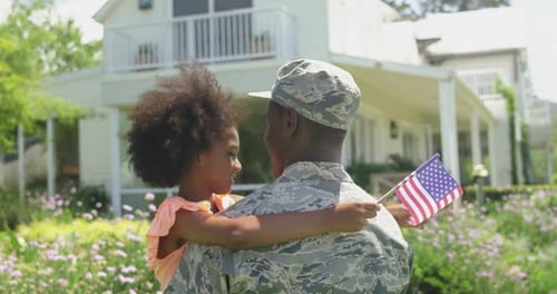 Soldier Hugs Daughter Holding American Flag in Garden