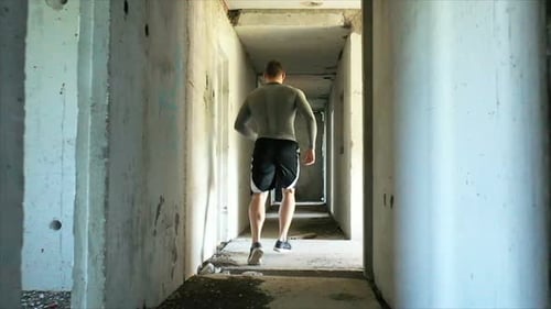 Plan de suivi d'un athlète masculin anonyme courant dans le couloir sombre d'un bâtiment abandonné pendant une période intense