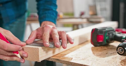 Adult Measures Wood Plank at Workbench with Ruler