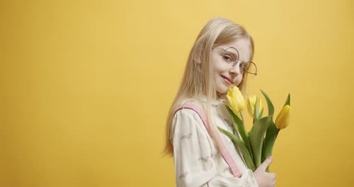 Blonde Child Holding Yellow Tulips on Yellow Background