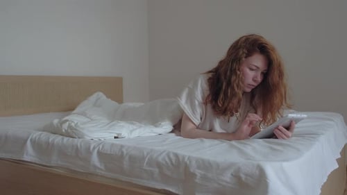 Young Woman Uses Tablet While Lying in Bed