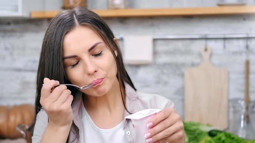 Young Woman Eating Yogurt in Kitchen