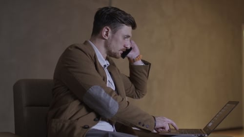 Man Using Laptop, Talking on Cell Phone Indoors