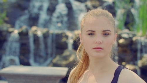 Blonde Woman Posing In Park. Young Woman Portrait Near Waterfall