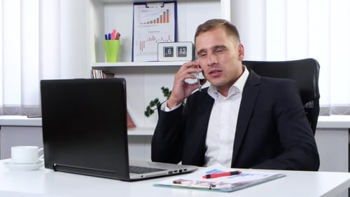 Man Working on Laptop and Speaking on Phone