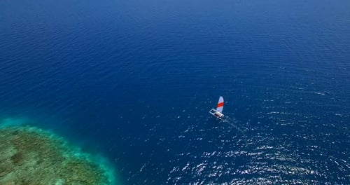 Aerial drone view of a man and woman sailing on a boat to a tropical island.