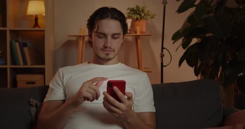 Crop View of Young Man Scrolling Smartphone Screen While Sitting on Couch at Home in Evening
