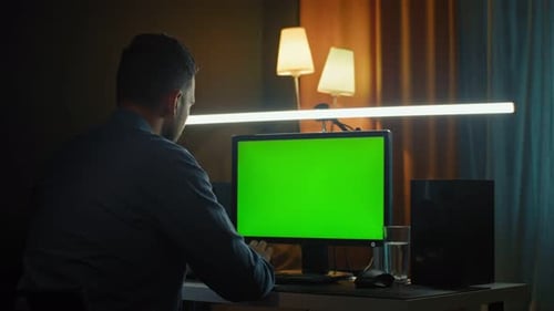 Young Professional Creative Employee Works on His Personal Computer with Big Green Screen Mock Up