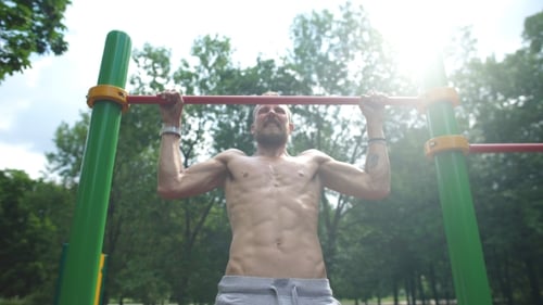 Young Man Doing Pull Ups On Horizontal Bar Outdoors