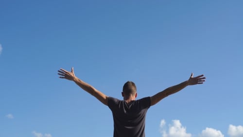 Man Standing Outside, Arms Raised to Blue Sky