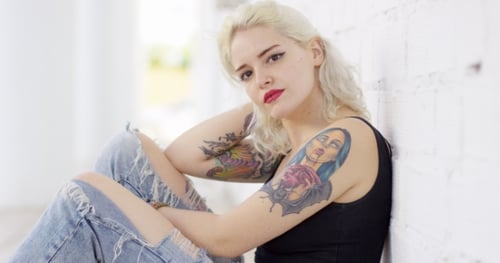 Young Woman with Tattoos Posing Against White Brick Wall