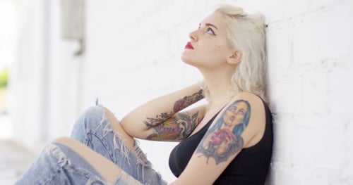 Woman with Tattoos Sitting Against White Brick Wall