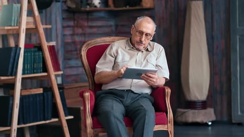 Senior Man Uses Tablet in Armchair