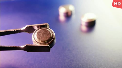 Button Battery Held by Metal Tweezers Close Up