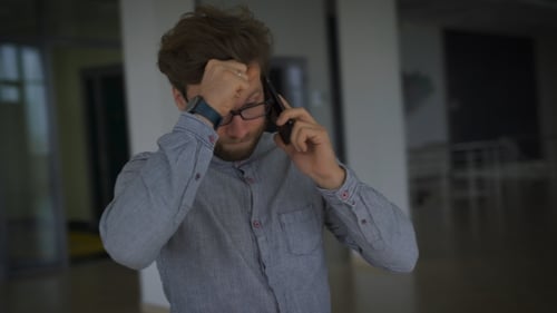 Young Man With Glasses Standing In The Room And Very Upset Talking On Cell Phone.