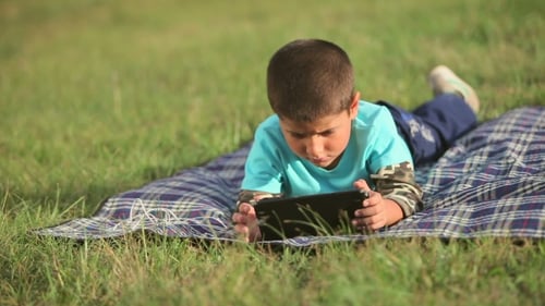 Boy Playing On The Lawn With a Tablet
