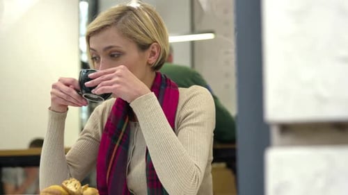 Woman in cafe drinking coffee and using mobile phone.
