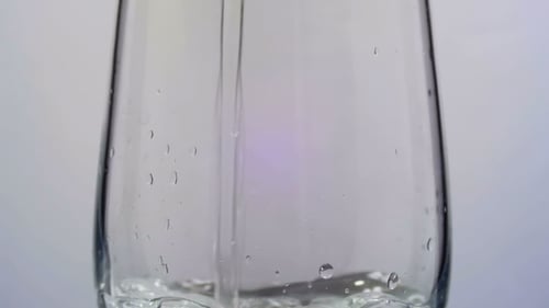 El agua se vierte en un vaso transparente sobre un fondo blanco.