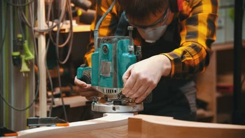 Carpentry Indoors - a Man Woodworker Polishes a Corner of a Wooden Part of a Furniture