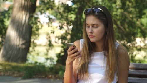 Mujer joven en un banco del parque con su teléfono