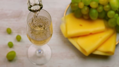 White Wine Pouring into Glass with Cheese and Grapes