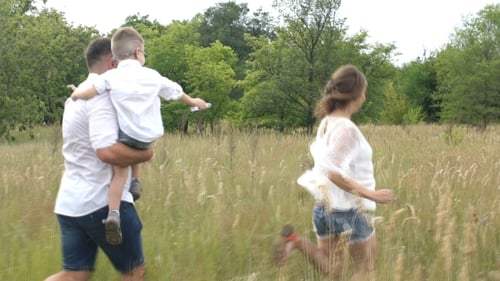 Family Running Through Tall Grass in Sunny Field
