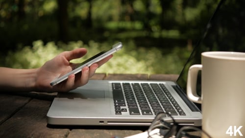 Using Smartphone with Laptop and Coffee Outdoors