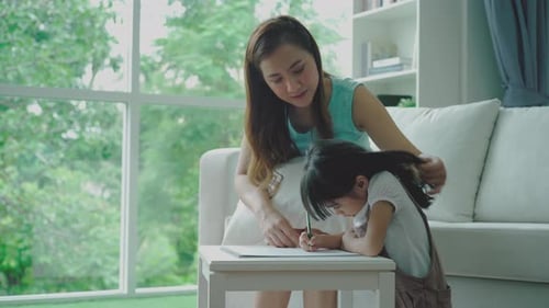 Heimstudienkonzept: Eine schöne alleinerziehende asiatische Mutter bringt ihrer Tochter Lesen, Schreiben und Zeichnen bei