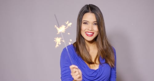 Happy Young Woman Holding a Sparkler Indoors