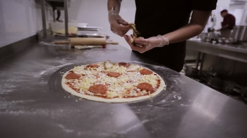 Koch macht italienische Pizza. Hände des Küchenchefs Fügen Sie die Zutaten in The Pizza
hinzu