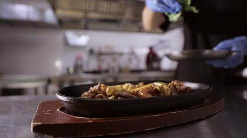 Chef Adding Herbs to Pan With Vegetables and Meat on Wooden Stand