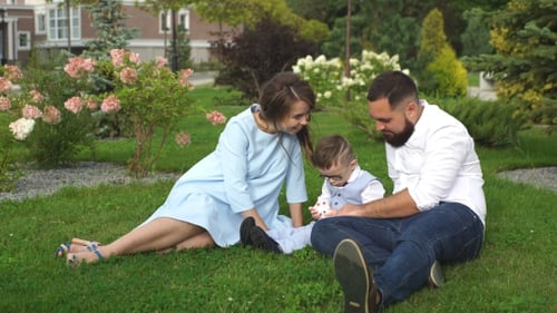 Happy Family Sitting On The Grass In The Park