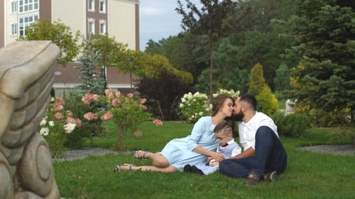 Happy Family Sitting On The Grass In The Park