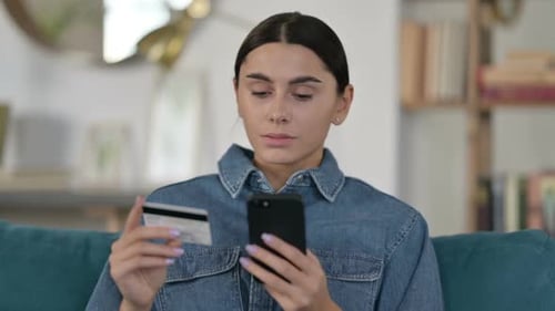 Young Woman Frowning While Using Credit Card on Phone