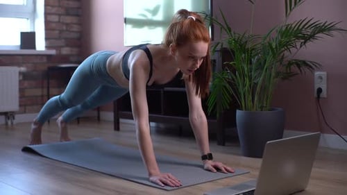 Junge Fitnessfrau trainiert zu Hause auf dem Boden und schaut sich Online-Videos auf einem Laptop an