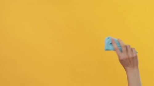 Hand Wipes a Yellow Surface with Blue Cloth