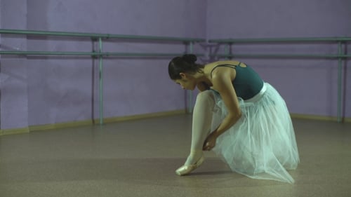 Ballerina Puts on Ballet Shoes in Dance Studio