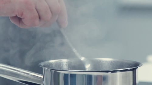 Person stirs simmering liquid in stainless steel pot