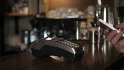 Customer Paying With NFC Technology By Mobile Phone On Terminal In Modern Cafe