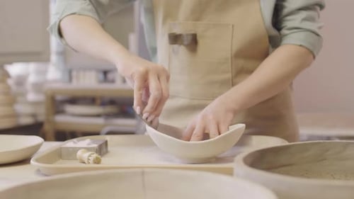 Woman smoothing ceramic bowl with fingers and sponge