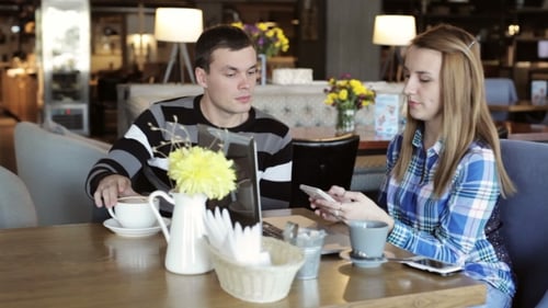 Boy and Girl in Cafe. People Use Laptop and Smartphones, Talk and Drink Coffee.