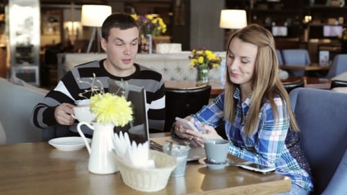 Boy And Girl In Cafe. People Use Laptop And Smartphones, Talk And Drink Coffee