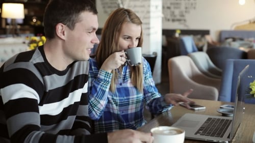 Boy and Girl in Cafe. People Use Laptop and Smartphones, Talk and Drink Coffee.