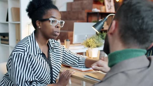 Ambitious AfroAmerican Lady Discussing Business with Male Colleague Caucasian Man in Office in