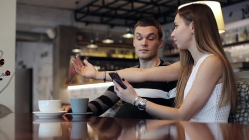 Attractive Young Couple Talking and Using Smartphone at Cafe