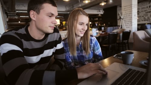 Two Friends Sitting in Cafe, Talking, Drinking Coffee and Using Laptop